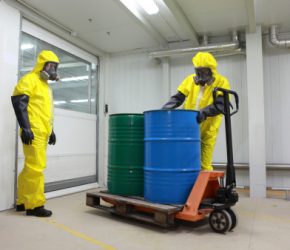 Two specialists in protective uniforms,masks,gloves and boots  dealing with barrels of chemicals on forklift in factory